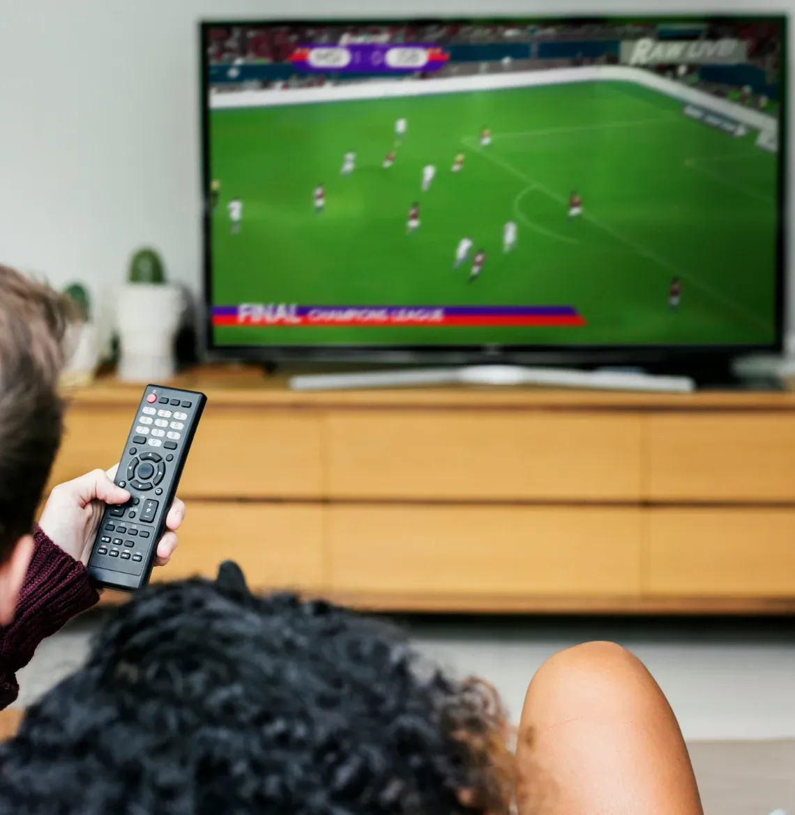 Dos personas viendo un partido de fútbol en vivo por televisión en casa